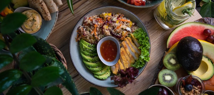 A high angle shot of plates of salad and fresh fruits and vegetable on a wooden surface